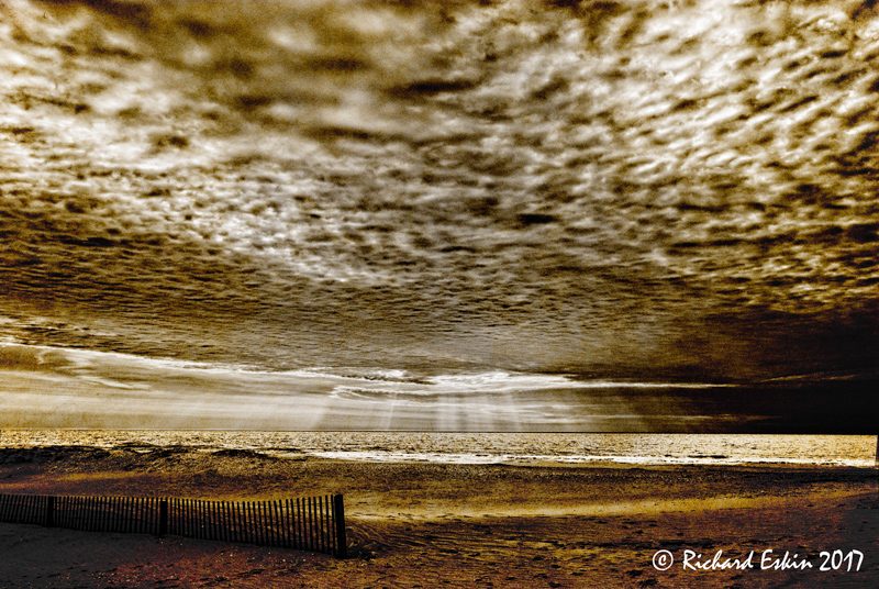 A beach at sunrise with rays hitting on the water and a beautiful cloud formation.