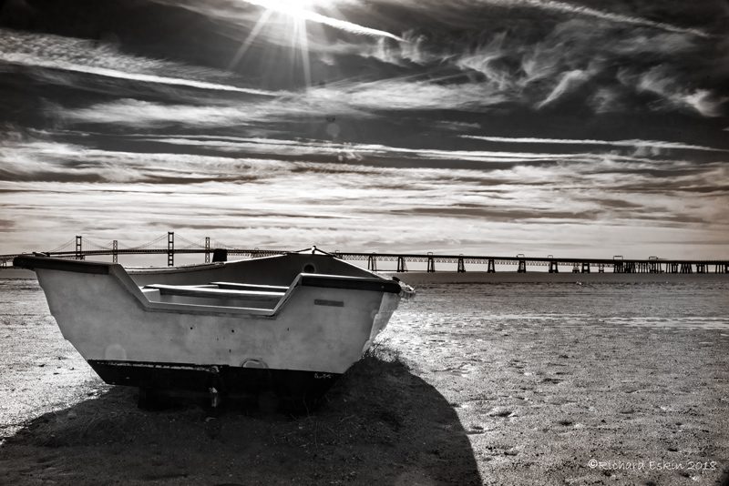 A small boat on the beach with the Bay Bridge in the background.